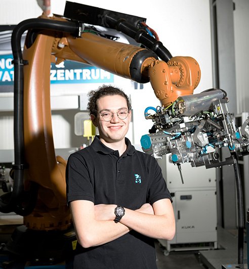 A dual student in mechatronics stands in front of an industrial robot.